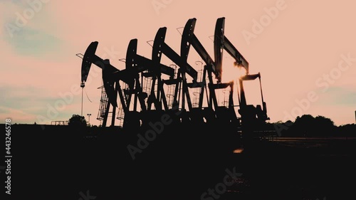 Silhouette of oil extracting operation by pump jack in the oil field