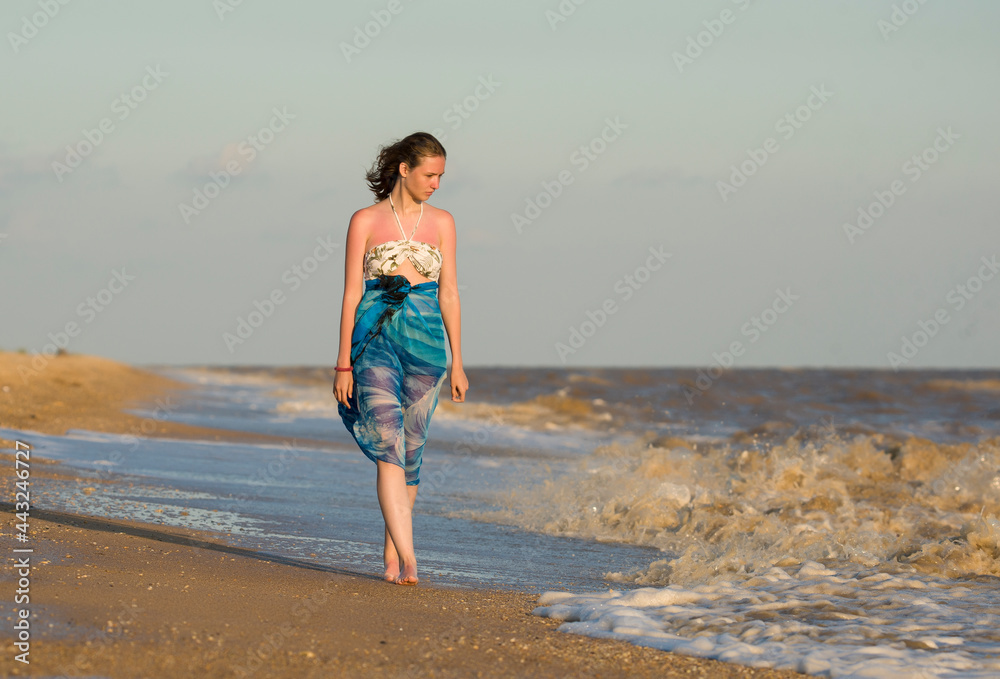 a girl walks along the seashore barefoot and looks into the distance
