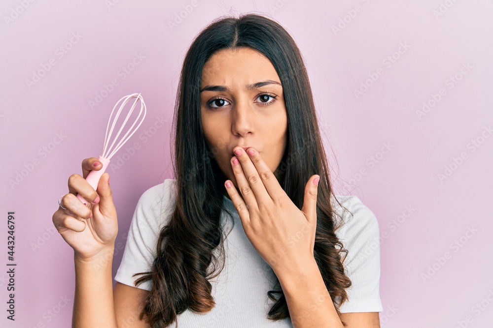 Young hispanic woman holding whisk covering mouth with hand, shocked and afraid for mistake. surprised expression Young hispanic woman holding whisk covering mouth with hand, shocked and afraid for mistake. surprised expression