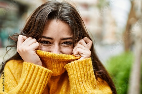 Young beautiful brunette woman wearing turtleneck sweater doing funny gesture covering face with sweater