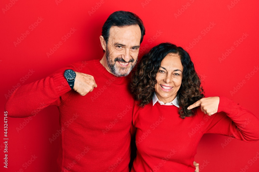 Middle age couple of hispanic woman and man hugging and standing together looking confident with smile on face, pointing oneself with fingers proud and happy.
