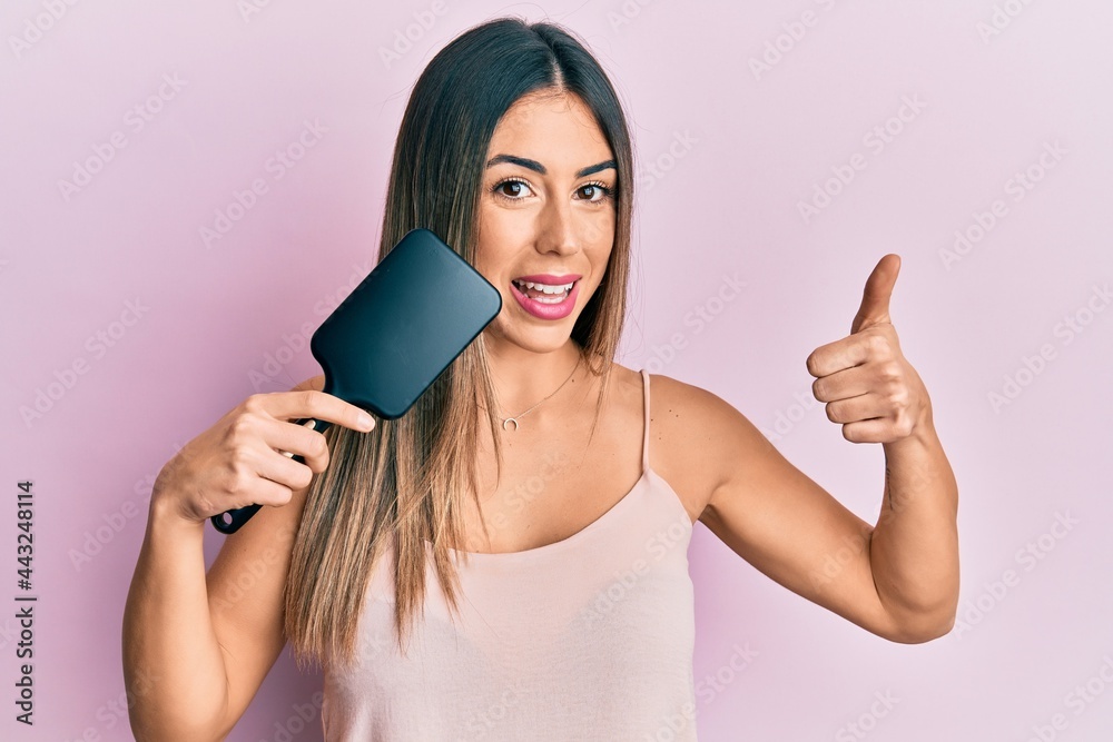 Young hispanic woman styling hair using comb smiling happy and positive, thumb up doing excellent and approval sign Young hispanic woman styling hair using comb smiling happy and positive, thumb up doing excellent and approval sign