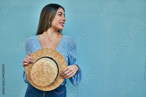 Young hispanic woman smiling happy holding summer hat at the city.