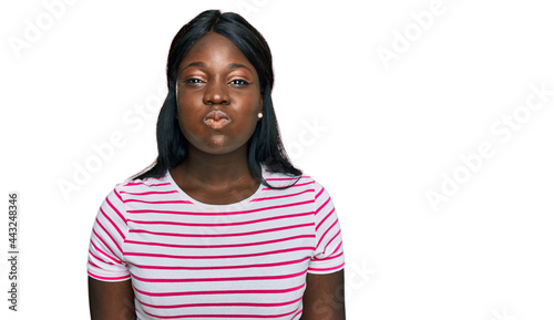 African young woman wearing casual striped t shirt puffing cheeks with funny face. mouth inflated with air, crazy expression.