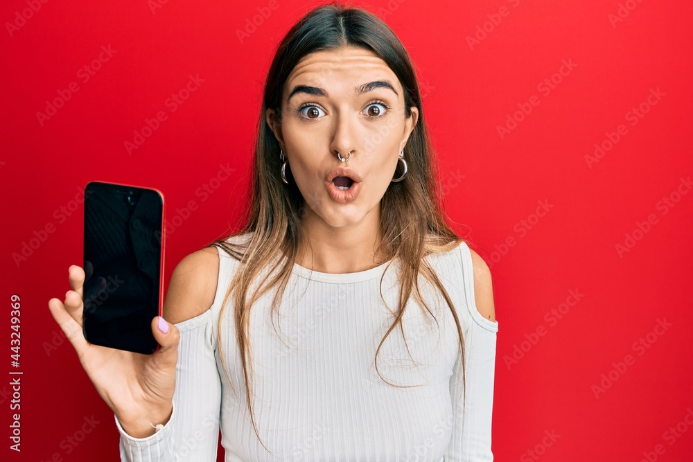 Young hispanic woman holding smartphone showing blank screen scared and amazed with open mouth for surprise, disbelief face Young hispanic woman holding smartphone showing blank screen scared and amazed with open mouth for surprise, disbelief face