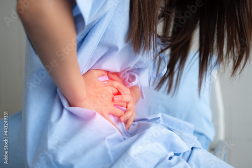 Unhappy Asian patient woman sitting on the hospital bed and holding on stomach suffering. Abdominal pain that comes from menstruation  diarrhea  or indigestion. Sickness and healthcare concept