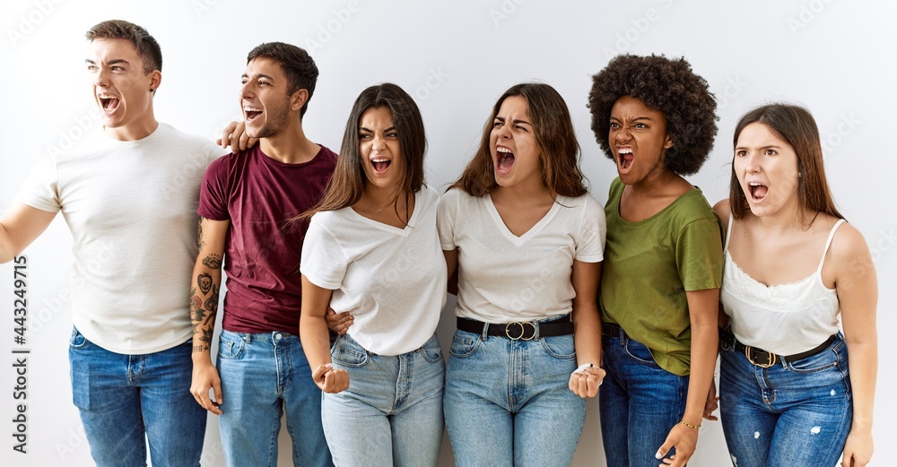 Obraz premium Group of young friends standing together over isolated background angry and mad screaming frustrated and furious, shouting with anger. rage and aggressive concept.