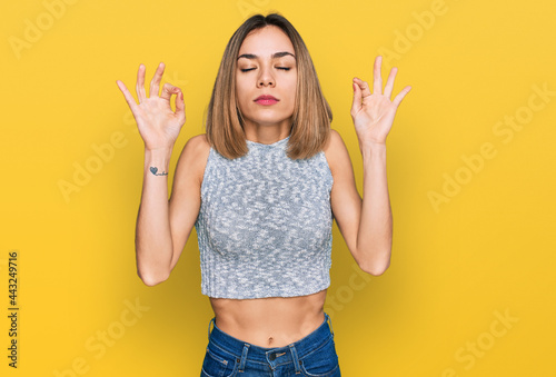 Young blonde girl wearing casual style with sleeveless shirt relax and smiling with eyes closed doing meditation gesture with fingers. yoga concept.