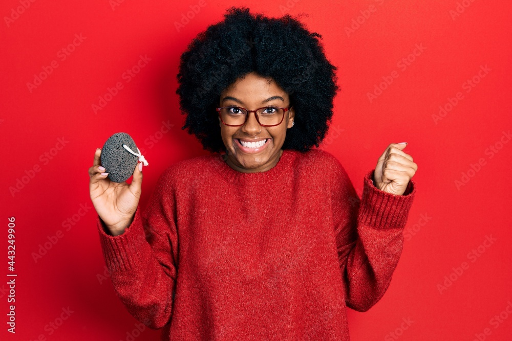 Young african american woman holding pumice stone screaming proud, celebrating victory and success very excited with raised arm Young african american woman holding pumice stone screaming proud, celebrating victory and success very excited with raised arm