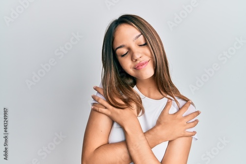 Young brunette woman wearing casual white t shirt hugging oneself happy and positive, smiling confident. self love and self care