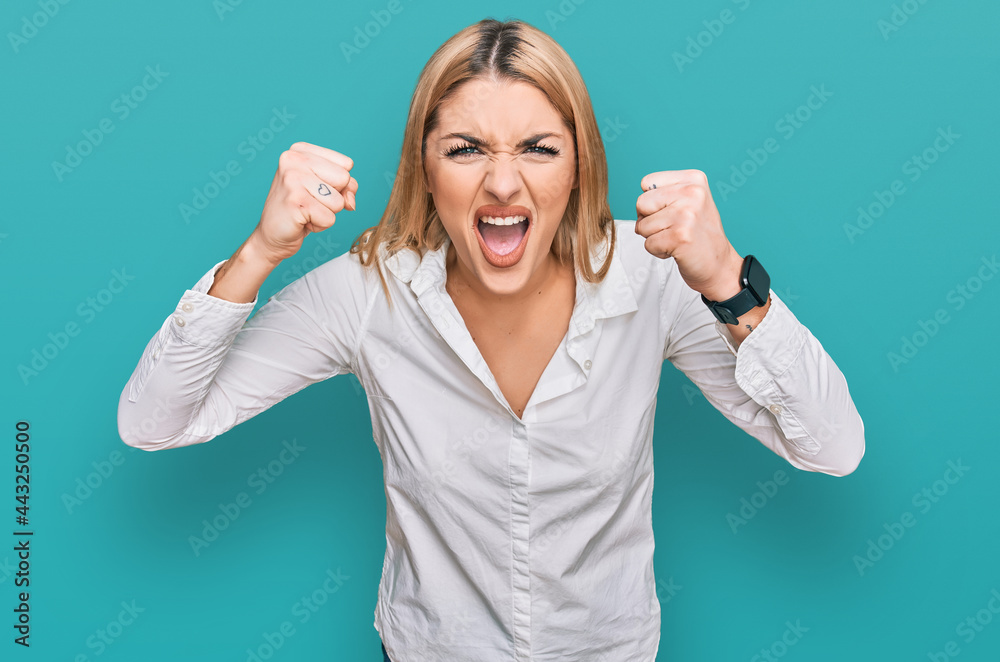 Young caucasian woman wearing casual clothes angry and mad raising fists frustrated and furious while shouting with anger. rage and aggressive concept. - obrazy, fototapety, plakaty 