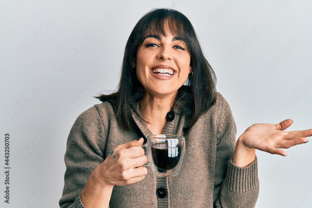 Young hispanic woman drinking a cup of coffee celebrating achievement with happy smile and winner expression with raised hand Young hispanic woman drinking a cup of coffee celebrating achievement with happy smile and winner expression with raised hand