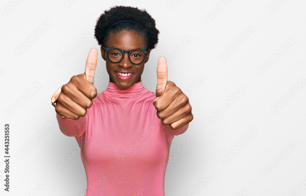 Young african american girl wearing casual clothes and glasses approving doing positive gesture with hand, thumbs up smiling and happy for success. winner gesture. Young african american girl wearing casual clothes and glasses approving doing positive gesture with hand, thumbs up smiling and happy for success. winner gesture.