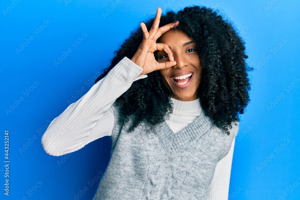 African american woman with afro hair wearing casual winter sweater doing ok gesture with hand smiling, eye looking through fingers with happy face. African american woman with afro hair wearing casual winter sweater doing ok gesture with hand smiling, eye looking through fingers with happy face.
