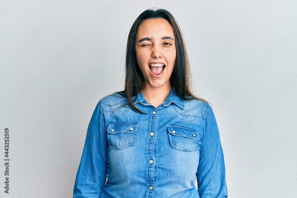 Young hispanic woman wearing casual denim jacket winking looking at the camera with sexy expression, cheerful and happy face. Young hispanic woman wearing casual denim jacket winking looking at the camera with sexy expression, cheerful and happy face.