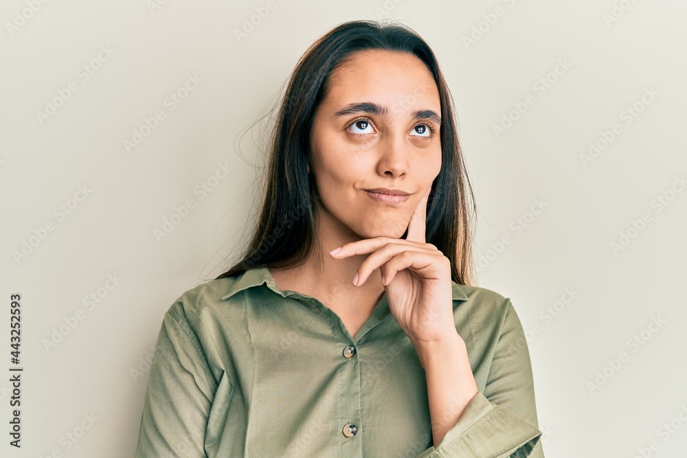 Young hispanic woman wearing casual clothes serious face thinking about question with hand on chin, thoughtful about confusing idea Young hispanic woman wearing casual clothes serious face thinking about question with hand on chin, thoughtful about confusing idea