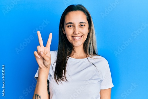 Young hispanic woman wearing casual white t shirt showing and pointing up with fingers number two while smiling confident and happy.