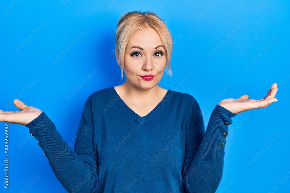 Young blonde woman wearing casual blue sweater clueless and confused with open arms, no idea and doubtful face. Young blonde woman wearing casual blue sweater clueless and confused with open arms, no idea and doubtful face.