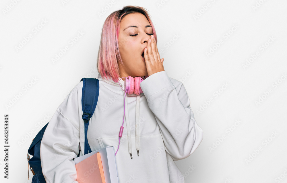 Hispanic woman with pink hair wearing student backpack and headphones bored yawning tired covering mouth with hand. restless and sleepiness. Hispanic woman with pink hair wearing student backpack and headphones bored yawning tired covering mouth with hand. restless and sleepiness.
