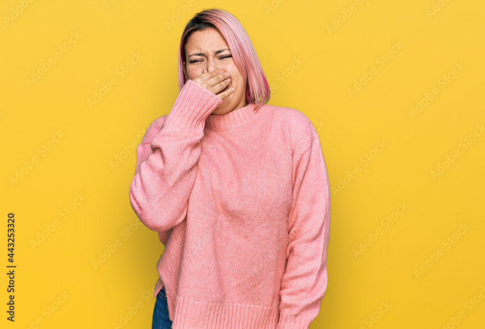 Hispanic woman with pink hair wearing casual winter sweater smelling something stinky and disgusting, intolerable smell, holding breath with fingers on nose. bad smell Hispanic woman with pink hair wearing casual winter sweater smelling something stinky and disgusting, intolerable smell, holding breath with fingers on nose. bad smell