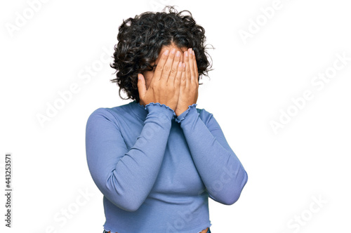 Young hispanic woman with curly hair wearing casual clothes with sad expression covering face with hands while crying. depression concept.