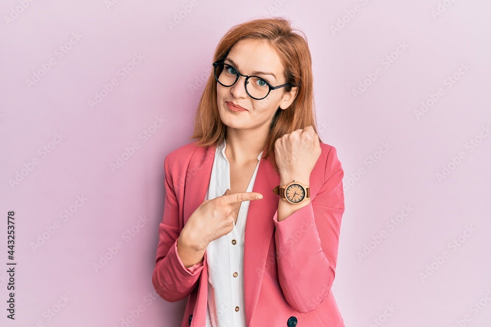 Young caucasian woman wearing business style and glasses in hurry pointing to watch time, impatience, looking at the camera with relaxed expression