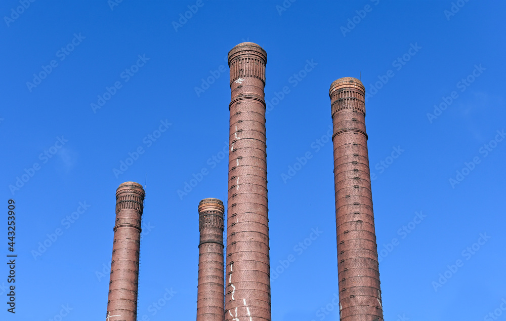 Ecology of large cities. Progress for a person. Smoke pipes made of bricks of an old city power plant against a blue sky background.