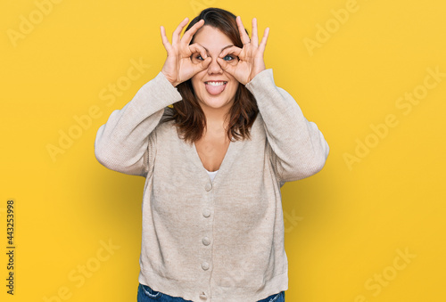Young plus size woman wearing casual clothes doing ok gesture like binoculars sticking tongue out, eyes looking through fingers. crazy expression.