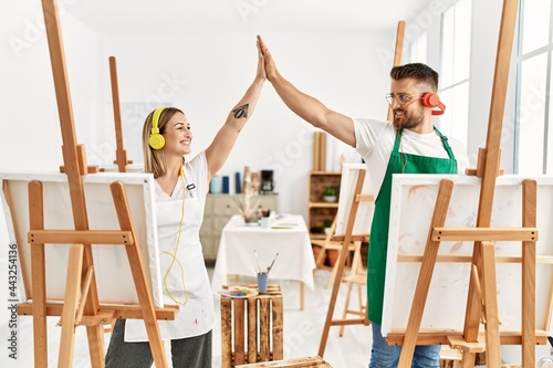 Young caucasian couple smiling happy listening to music high five at art studio.