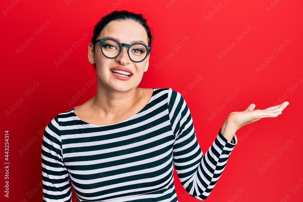 Young caucasian woman wearing casual clothes and glasses smiling cheerful presenting and pointing with palm of hand looking at the camera. Young caucasian woman wearing casual clothes and glasses smiling cheerful presenting and pointing with palm of hand looking at the camera.