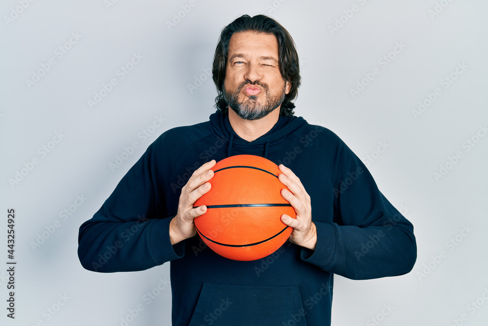 Middle age caucasian man holding basketball ball looking at the camera blowing a kiss being lovely and sexy. love expression.