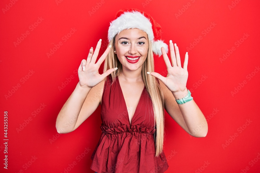 Young blonde girl wearing christmas hat showing and pointing up with fingers number nine while smiling confident and happy.