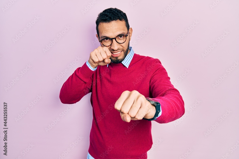 Hispanic man with beard wearing business shirt and glasses punching fist to fight, aggressive and angry attack, threat and violence Hispanic man with beard wearing business shirt and glasses punching fist to fight, aggressive and angry attack, threat and violence