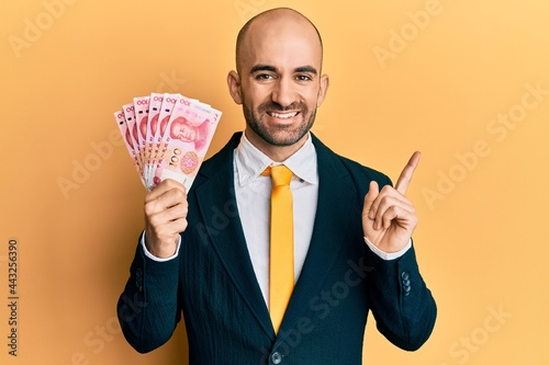 Young hispanic business man wearing business suit holding 100 yuan banknotes smiling happy pointing with hand and finger to the side