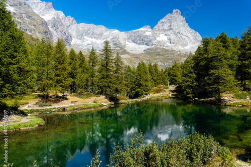 Panorama alpino con un laghetto circondato di abeti e le cime delle montagne sullo sfondo con il cielo azzurro in Valle d'Aosta, in Italia. Viaggiare. Vacanze. Settembre. In natura. Fuori.