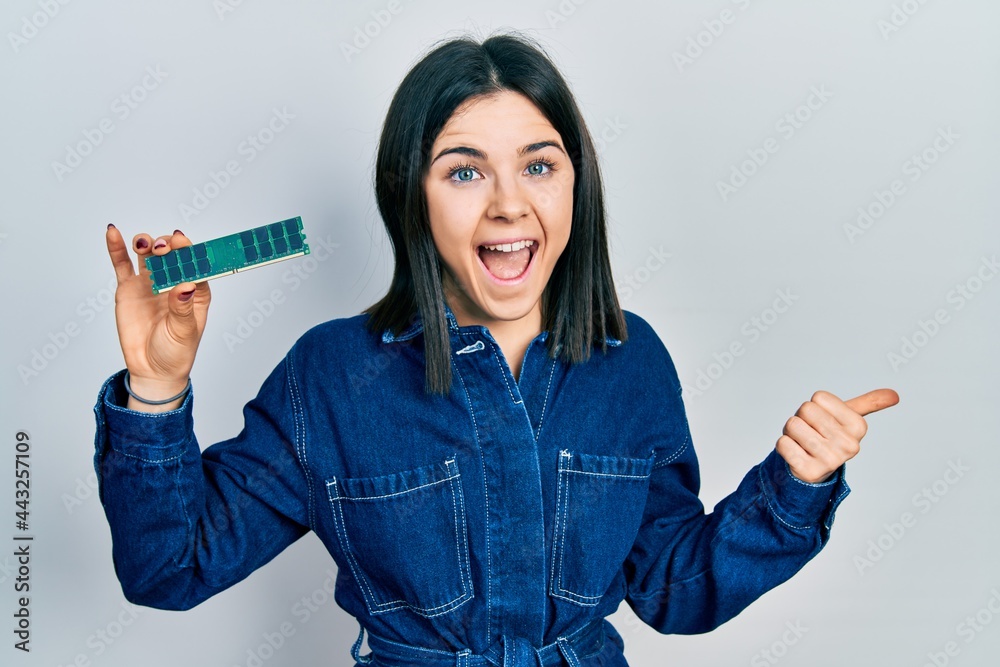 Obraz premium Young brunette woman holding computer ram pointing thumb up to the side smiling happy with open mouth