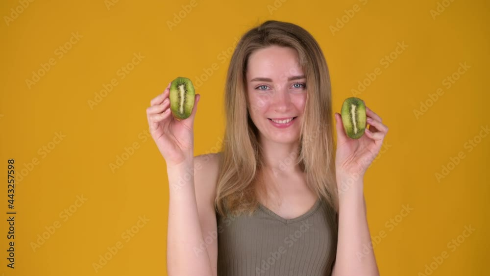 Smiling pretty young woman holding kiwi looking at camera isolated on yellow background. organic vegetables. Vegetarian concept. Smiling pretty young woman holding kiwi looking at camera isolated on yellow background. organic vegetables. Vegetarian concept.