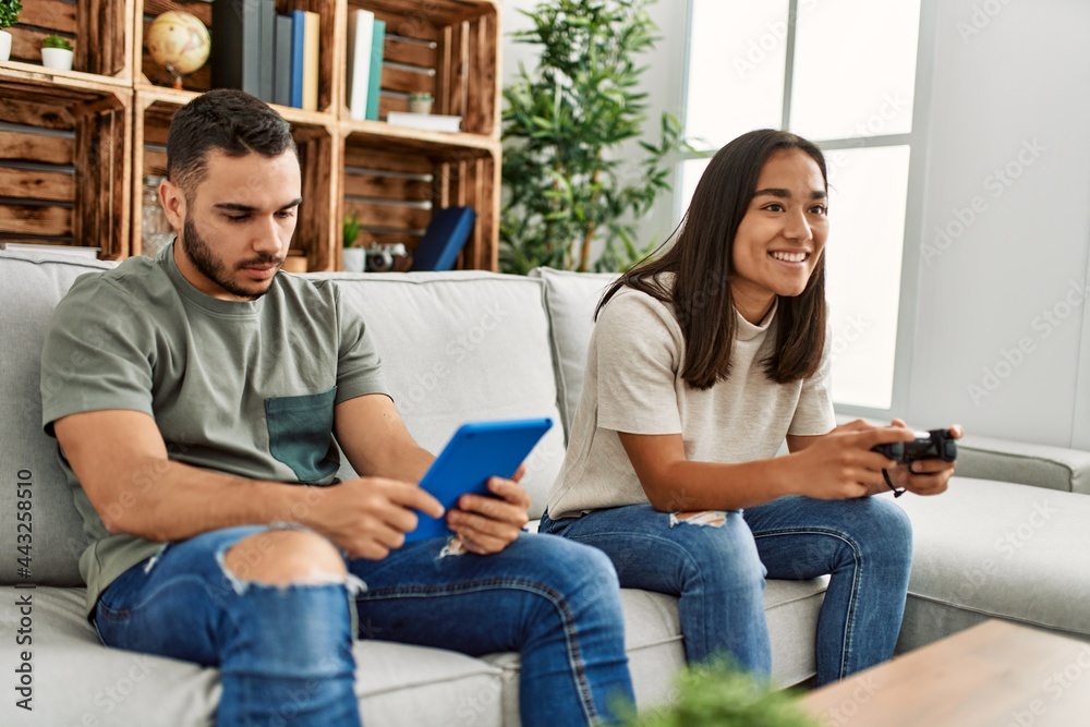Fototapeta premium Young latin couple playing video game and using touchpad at home.