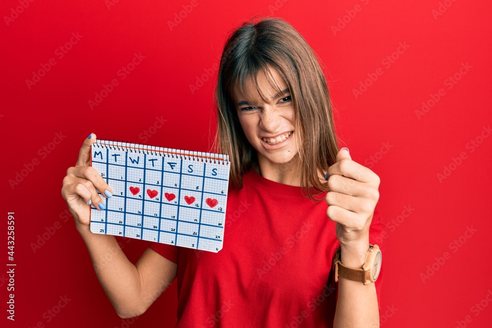 Teenager caucasian girl holding heart calendar annoyed and frustrated shouting with anger, yelling crazy with anger and hand raised Teenager caucasian girl holding heart calendar annoyed and frustrated shouting with anger, yelling crazy with anger and hand raised