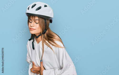Teenager caucasian girl wearing bike helmet with hand on stomach because indigestion, painful illness feeling unwell. ache concept.