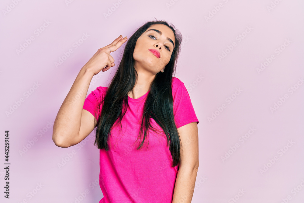 Young hispanic girl wearing casual pink t shirt shooting and killing oneself pointing hand and fingers to head like gun, suicide gesture. Young hispanic girl wearing casual pink t shirt shooting and killing oneself pointing hand and fingers to head like gun, suicide gesture.
