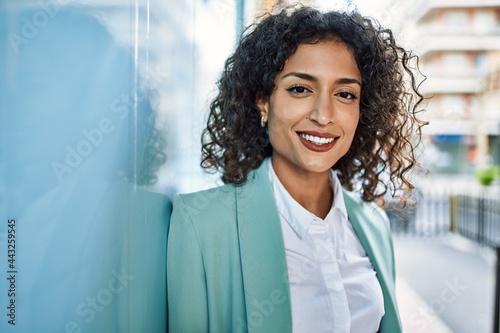 Young hispanic business woman wearing professional look smiling confident at the city leaning on the wall