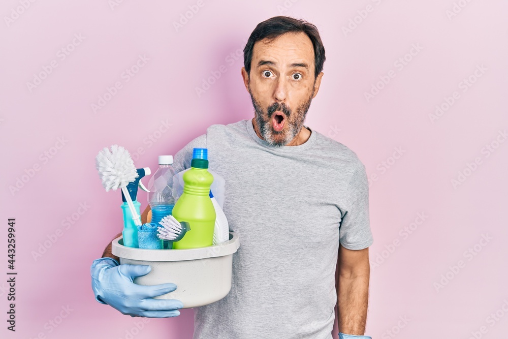 Middle age hispanic man holding cleaning products scared and amazed with open mouth for surprise, disbelief face Middle age hispanic man holding cleaning products scared and amazed with open mouth for surprise, disbelief face