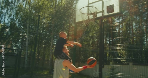 Happy family playing basketball, young sports father holding son on shoulders. Kid boy throwing ball in basketball hoop