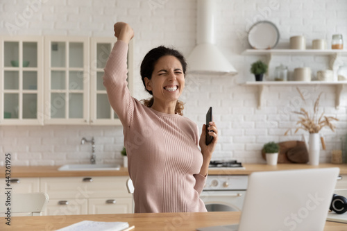 Overjoyed millennial sincere woman making yes gesture, holding smartphone in hands, celebrating online lottery giveaway victory notification, getting amazing win news, internet success concept.