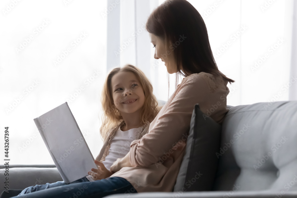 Curious little girl of elementary school age enjoy educational activity with caring mother tutor babysitter. Preteen schoolgirl sit on sofa discuss book with elder sister ask questions after reading Curious little girl of elementary school age enjoy educational activity with caring mother tutor babysitter. Preteen schoolgirl sit on sofa discuss book with elder sister ask questions after reading