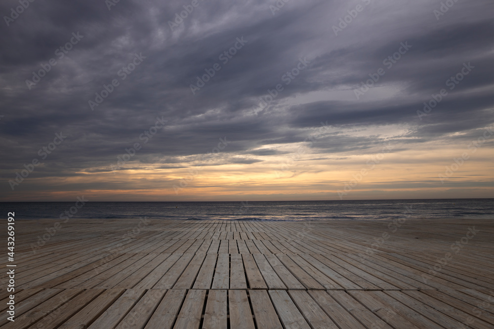 Imagen de una playa con unas tarimas de madera y al fondo un amanecer precioso