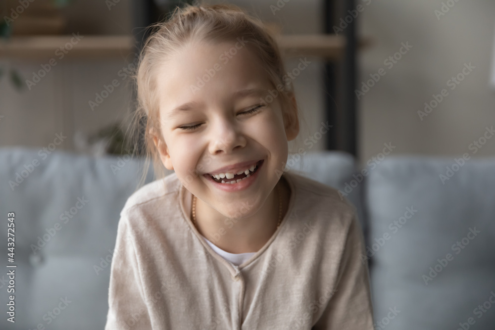 Sincere laughter. Overjoyed little girl sit on sofa at living room laugh with closed eyes to funny joke by video call. Joyful cute preteen kid having fun communicating with mate via virtual event app Sincere laughter. Overjoyed little girl sit on sofa at living room laugh with closed eyes to funny joke by video call. Joyful cute preteen kid having fun communicating with mate via virtual event app