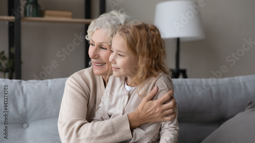 Dreaming together with granny. Dreamy little girl sit on knees of loving elderly grandmother look aside imagine visualize create fantasy future. Small child relax on mature nanny laps feel care safe