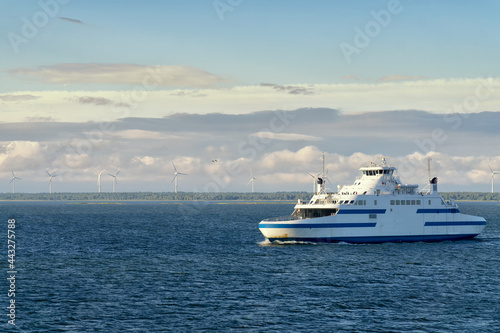 The small car ferry runs between Virtsu harbour Estonia and Saaremaa Island on Baltic Sea. Calm sea and blue sky with white clouds. In the background the wind farm on the seashore. © msnobody